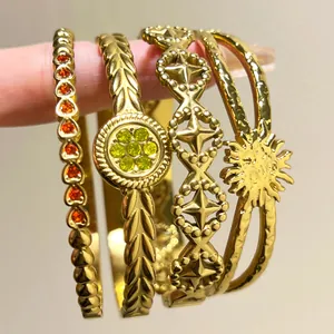 Close-up detail of four gold stainless steel bangles with various geometric patterns