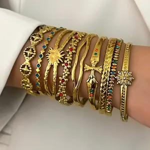 Detailed macro view of multiple gold stainless steel bracelets with sun and cross charms