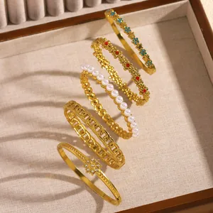 Detail of five gold stainless steel bangles with floral, pearl and hollow designs.