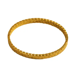 Detailed view of a golden stainless steel bangle featuring a textured chevron pattern