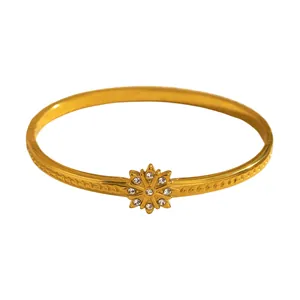 Close-up of gold-plated flower bangle featuring crystal accents and engraved leaf band
