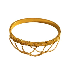 Close-up detail of gold-plated stainless steel bangle with leaf pattern and dangling chains