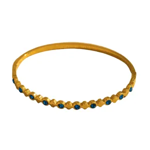 Detail view of a gold-plated geometric bangle featuring vibrant blue round stones