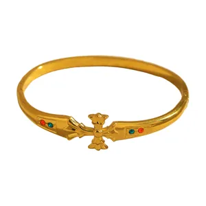 Close-up view of a luxury gold-plated cross bangle with red and teal stone accents.