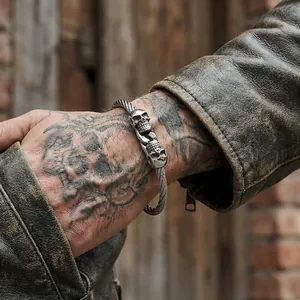 Detailed view of a gothic double skull stainless steel wire bracelet on a tattooed wrist