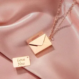 Close-up of rose gold envelope necklace with 'Love You' engraved card on pink silk.