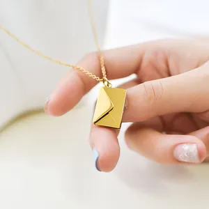 Detailed close-up of a golden stainless steel envelope pendant necklace held by a hand