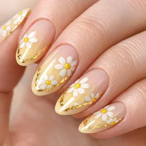 Close-up of almond press-on nails with white daisy patterns and gold foil flakes.