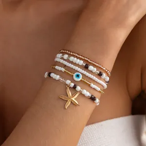 Close-up detail of a beaded bracelet set featuring a gold starfish and evil eye charm.