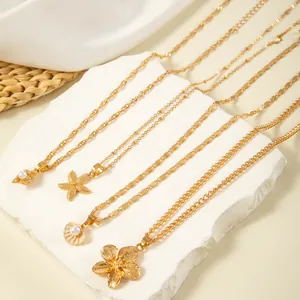 Close-up of golden necklaces featuring starfish, shell, and floral pendants on white stone.