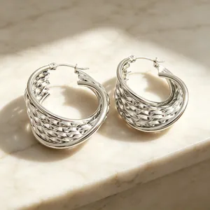Gros plan de boucles d'oreilles créoles en U en acier inoxydable avec texture tressée.