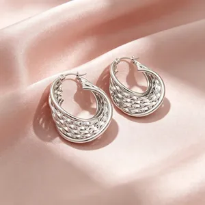 Gros plan de boucles d'oreilles créoles en U argentées avec texture tissée