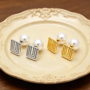 Detail of geometric square stainless steel earrings with large white pearls on a plate.