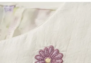 Gros plan d'une broderie florale violette sur une robe d'été en coton crème pour fille