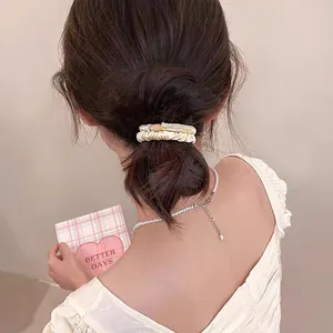 Détail d'un chouchou en satin crème sur une queue de cheval avec collier de perles
