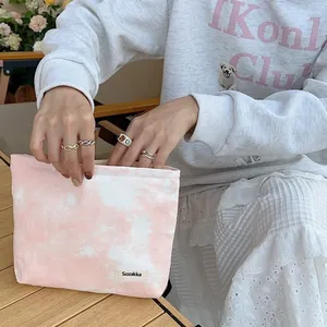 Pink tie-dye fabric makeup bag being opened by a model at a rustic wooden table