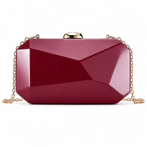 Close-up detail of a wine red geometric hard shell clutch bag featuring a gold metal chain strap