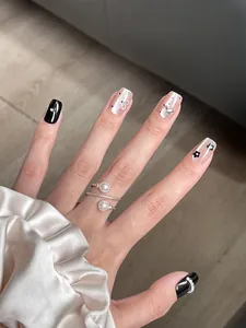 Detailed view of luxury black and nude press-on nails with floral and butterfly accents.