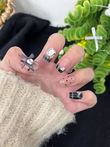 Close-up of black French style press-on nails with rhinestone and bow decorations