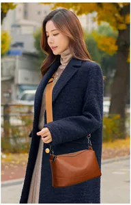 Detail view of a brown leather crossbody bag styled with a navy coat in autumn park