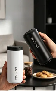 Detail showing hands holding minimalist black and white stainless steel coffee mugs in a cozy setting