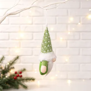 Close-up of a green knitted Christmas gnome ornament hanging from a white branch