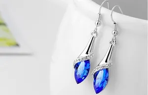 Detailed view of silver drop earrings with dark blue crystals on a white ceramic cup