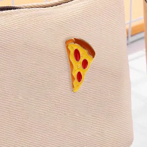 Close-up of a pizza slice enamel pin with yellow cheese on beige canvas bag
