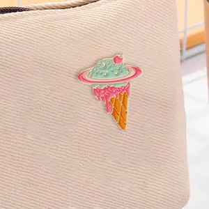 Detail of mint green planet ice cream enamel pin on a beige canvas bag fabric