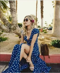 Blue V-neck maxi dress with white polka dots shown in a sunny outdoor palm park setting