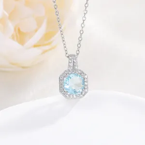 Close-up of silver necklace with round light blue zircon pendant and halo stones