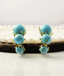 Detail view of turquoise earrings with three blue beads on a premium wooden prop
