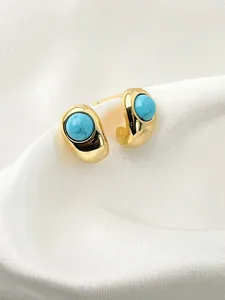 Close-up of gold turquoise stud earrings on white silk fabric with elegant lighting