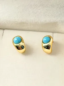 Macro close-up of small turquoise stud earrings with polished gold-tone metal bezel