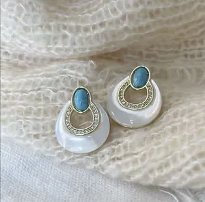 Detail of vintage round turquoise earrings with gold rim on white knit background