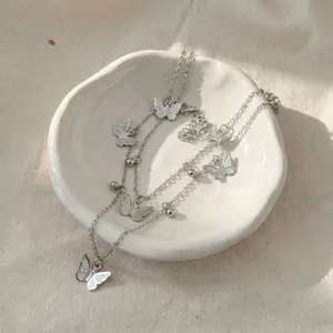 Detailed macro view of silver-toned double-layered butterfly necklace on white ceramic dish