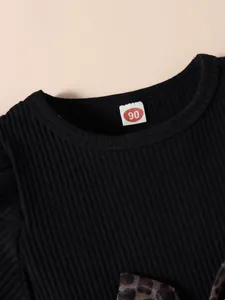 Close-up detail of black ribbed cotton girl's dress neckline featuring leopard bow.