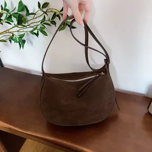 Close-up view of a dark brown suede dumpling hobo bag held over a rustic wooden bench