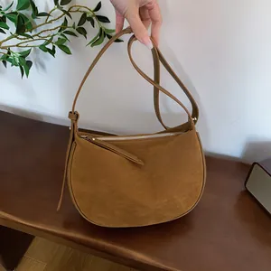 Detailed handheld view of a brown suede crescent shoulder bag over a wooden bench.
