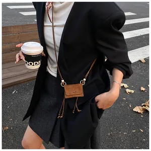 A model wearing a retro brown suede mini coin purse with a minimalist cord strap