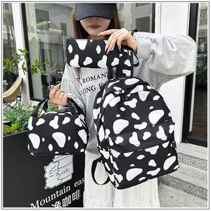 Model holding a 3-piece cow print bag set including a backpack, lunch bag, and pouch
