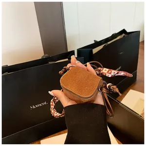 A detailed close-up of a retro brown suede mini coin purse with a patterned lanyard