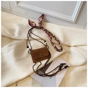 Detail of a vintage brown suede mini crossbody bag with a decorative silk scarf and wooden bead strap