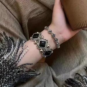 Detailed close-up of vintage rose and black square gemstone bracelets on a wrist.