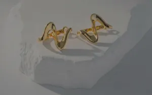 Close-up of wavy gold metal ear cuff jewelry on a white textured stone background.