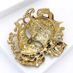 Detailed back view of a gold alloy carnival mask brooch with red enamel detailing.