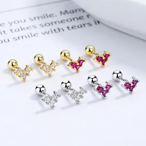 Close-up of heart-shaped screw back earrings in gold and silver with red and white gems.