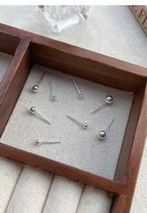 Detail view of minimalist S999 sterling silver ball stud earrings in a wooden jewelry tray