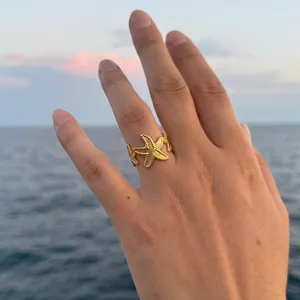 Λεπτομέρεια ενός χρυσού δαχτυλιδιού αστερία στο χέρι με φόντο τον ωκεανό