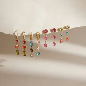 Macro detail of various colorful geometric zircon drop earrings hanging from a paper edge